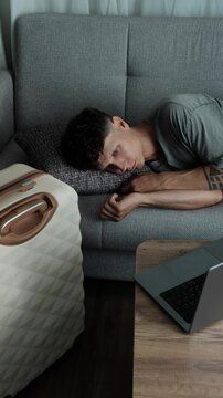 Life on hold between moves. Man lying on sofa in temporary apartment staring into space, feeling uncertain about the future. Vertical video