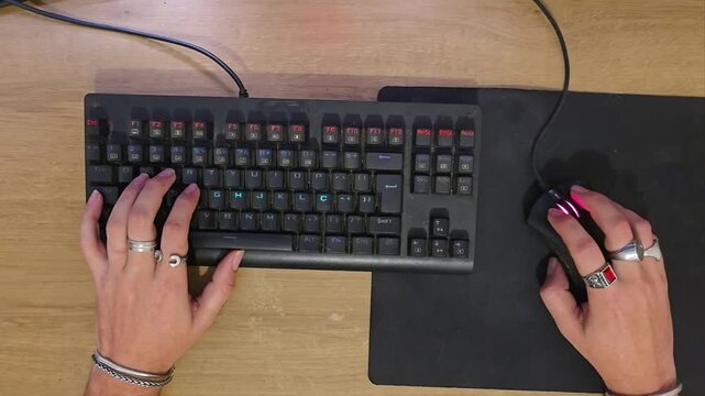 Top-down view of gamer hands typing on mechanical keyboard and clicking mouse during PC gameplay