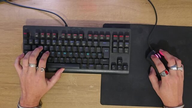 Top-down view of gamer hands typing on mechanical keyboard and clicking mouse during PC gameplay