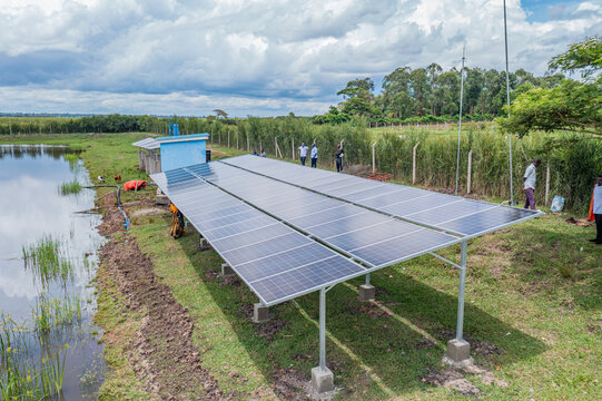 Aerial view of solar panels installed near a pond with people standing nearby in a rural landscape in Kumi, Eastern Region, Uganda.