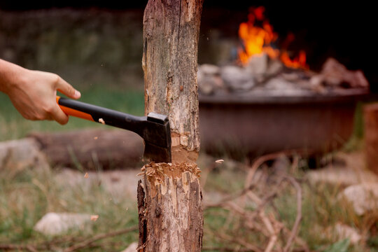 a person's hand using a hatchet to chop a log in front of a burning campfire in nature, concept of bushcraft, concept of survival, concept of camping