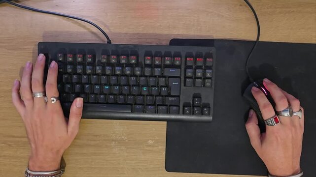 Top-down view of gamer hands typing on mechanical keyboard and clicking mouse during PC gameplay