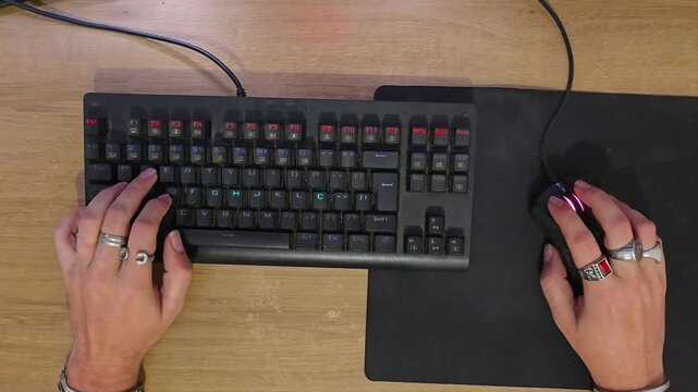 Top-down view of gamer hands typing on mechanical keyboard and clicking mouse during PC gameplay