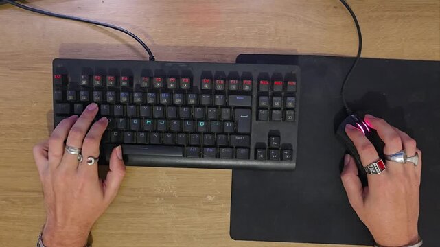 Top-down view of gamer hands typing on mechanical keyboard and clicking mouse during PC gameplay