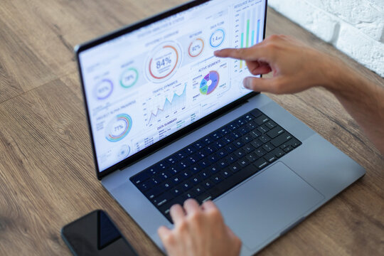 Close-up of a person's hands analyzing business data and metrics on a laptop screen with graphs and charts. Modern workspace. Businessman working