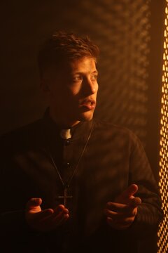 Priest talking to parishioner near wooden window in confessional booth