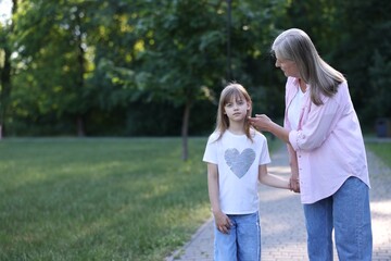 Fototapeta premium Grandmother and granddaughter holding hands while walking in summer park. Space for text
