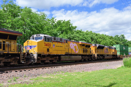 Multiple Union Pacific Railroad locomotives, including one sporting a special breast cancer awareness banner, lead a container train westbound through west suburban Chicago.