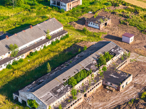 Aerial view of abandoned industrial buildings with damaged roofs and overgrown vegetation surrounded by rural fields in Lublewo Leborskie, Wojewodztwo pomorskie, Poland.
