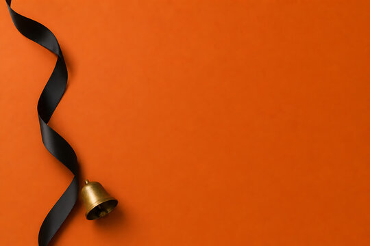 Small brass bell attached to a decorative black ribbon on an orange background for halloween greeting cards with empty copy space halloween greeting seasonal celebration decoration background