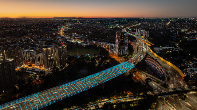 Aerial view of the illuminated Citylink Sound Tube at sunset, featuring urban infrastructure, high-rise buildings, and glowing traffic lights in Flemington, Victoria, Australia.