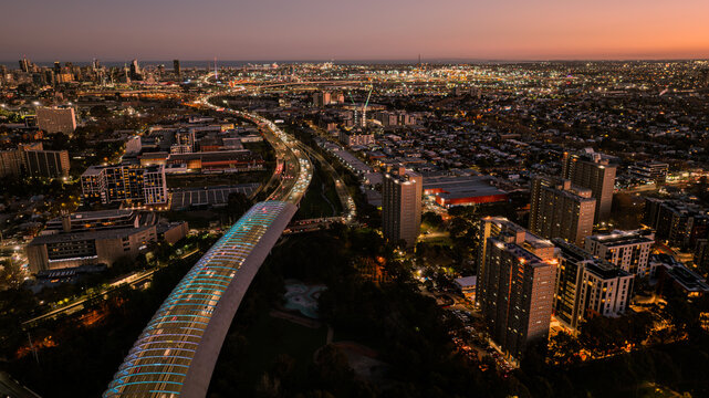 Aerial view of the illuminated Citylink Sound Tube stretching across the urban landscape at dusk, with highway traffic and city lights in Flemington, Victoria, Australia.