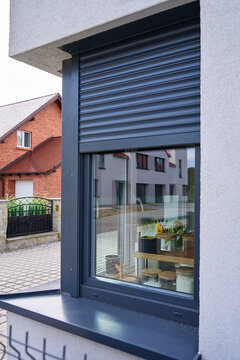 Dark gray roller shutter is lowered above kitchen window, with storage jars and flowers visible inside