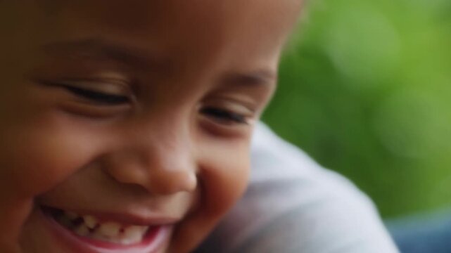 Smiling child laughing with bright eyes, raised cheeks, visible dimples, and open expression against soft blurred green background in close view, with child, smile, laughing, teeth detail