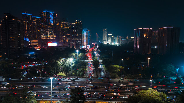 Aerial view of illuminated skyscrapers and heavy traffic on a multi-lane highway at night in Jakarta, Indonesia.