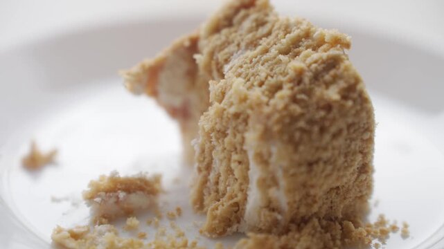 Fork breaks off piece of layered honey cake, showing cream layers and crumbs. Homemade dessert and cake serving