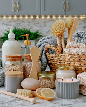 A cozy collection of spa and self-care items arranged in a warm, inviting setting. Featured are a candle, soaps, lotions, brushes, and jars filled with natural ingredients.