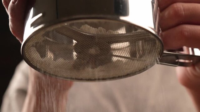 Close-up of flour being sifted through a sieve cup in slow motion.