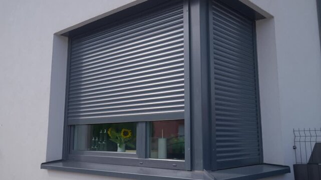 Roller shutter rises over house window, revealing more of the glass below. Concept of exterior shading control and privacy