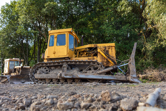 View of a yellow bulldozer parked on a dirt ground in front of a dense forest in Kelme, Siauliai County, Lithuania.