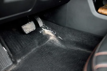 Close view of vehicle driver footwell showing scattered white powder on dark carpet near brake and accelerator pedals under soft interior light, with car, vehicle, interior, footwell detail © Евгений Вершинин