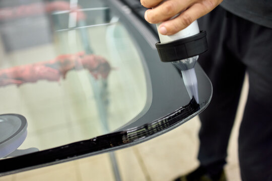 Technician polishing glossy black car hood with rotary buffer in bright auto repair workshop under reflective lighting, with car, hood, polishing, technician detail