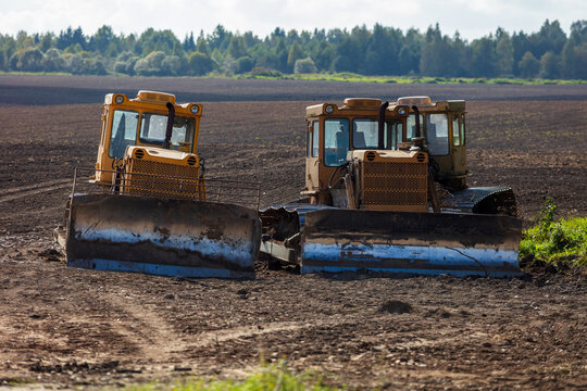 View of two yellow bulldozers parked in a large plowed field with a forest in the background in Kelme, Siauliai County, Lithuania.