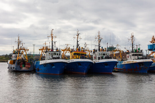 View of several fishing boats moored side by side in the harbor with masts and colorful hulls under a cloudy sky in Klaipeda, Klaipeda County, Lithuania.