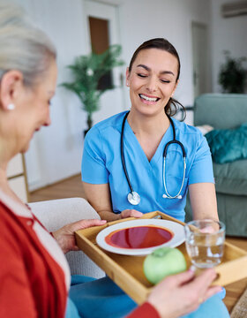 Doctor or nurse caregiver serving a meal to senior woman at home or nursing home