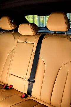 Rear leather car seats with center armrest, three headrests, visible seatbelt buckles, decorative stitching, textured upholstery, and compact modern vehicle interior details