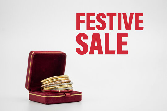 An open golden jewelry gift box with red velvet lining contains a stacked group of gold silver and rose gold bangles with green and red gems next to the bold red text that says FESTIVE SALE