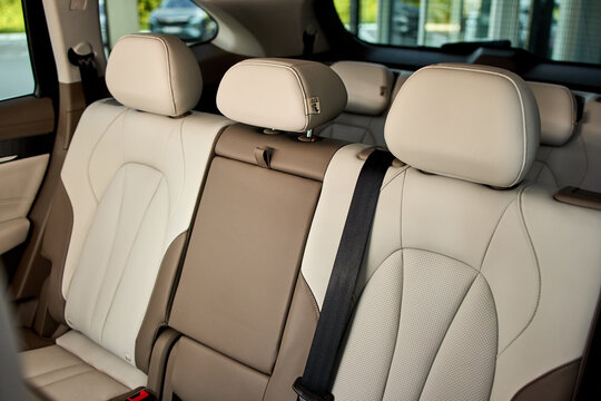 Rear leather car seats with center armrest, three headrests, visible seatbelt buckles, decorative stitching, textured upholstery, and compact modern vehicle interior details