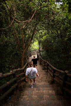 View of two people hiking down the stone stairs of The Marble Mountains surrounded by lush forest and trees in Da Nang, Da Nang, Vietnam.