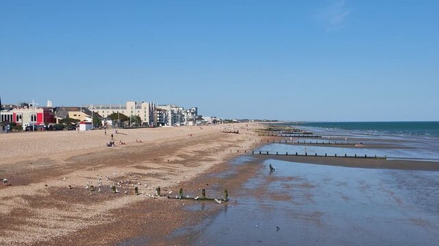 Bognor Regis west sussex England UK. 14.07.2026. Video. A wide shot of a bustling pebble beach on a clear day, featuring diverse architecture and individuals relaxing by the sea at Bognor Regis 