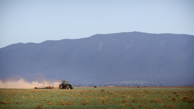 View of a tractor working in a field, kicking up dust, with mountains in the background in Port Augusta, South Australia, Australia.