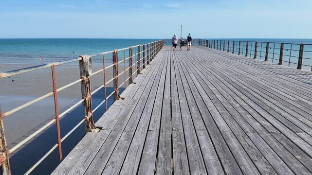 Bognor Regis West Sussex England UK. 14.07.2026. Video. A serene view of a long wooden pier extending into the calm blue sea, with a few people enjoying a leisurely stroll