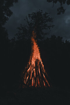 View of a large bonfire burning brightly in the night with tall flames illuminating the surrounding dark trees on Vormsi, Laane County, Estonia.