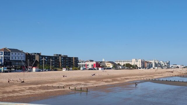 Bognor Regis West Sussex England UK. 14.07.2026. Video. A wide shot of a bustling pebble beach on a clear day, featuring diverse architecture and individuals relaxing by the sea at Bognor Regis 