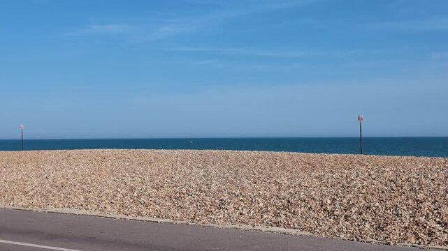 Bognor Regis West Sussex England UK. 14.07.2026. Video. A serene view of a road adjacent to a vast pebble beach leading to the tranquil blue sea on a bright sunny day