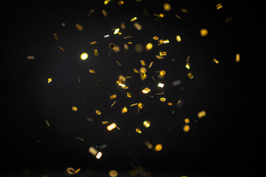 Numerous golden shiny confetti pieces in various shapes including rectangles circles and stars are gracefully falling and scattering through the air creating a festive and celebratory atmosphere