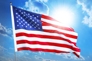 Fototapeta premium American flag waving against bright sun in blue sky