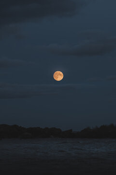 View of a bright full moon shining over the dark coastal landscape of Merikula, Harju maakond, Estonia.
