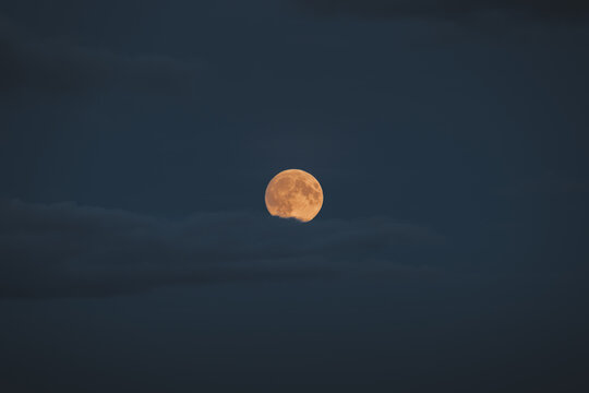 View of a golden full moon partially obscured by dark clouds in the night sky over Merikula, Harju maakond, Estonia.