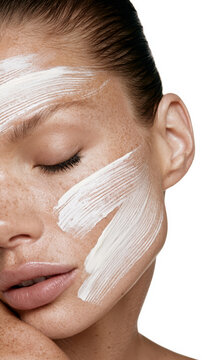 Woman with closed eyes and natural freckles applying a white facial mask onto her skin, representing beauty, skincare, hydration, and self care for healthy skin