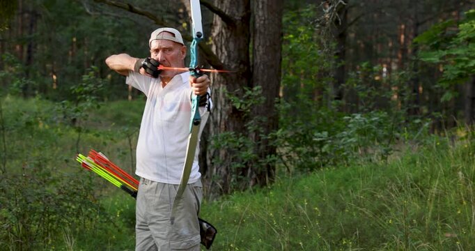 Senior man practicing recurve archery in forest during outdoor training