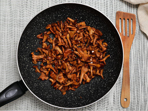 Fried chanterelle mushrooms Cantharellus cibarius in black frying pan with wooden spatula