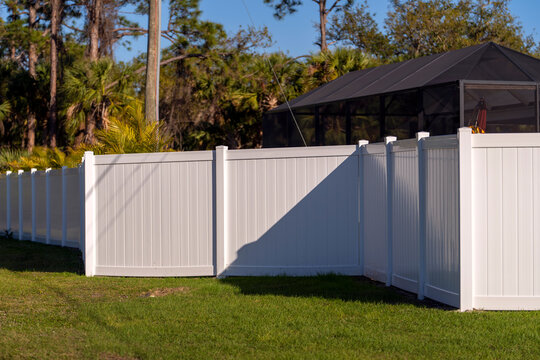 White vinyl picket fence on green lawn surrounding property grounds for backyard protection and privacy.