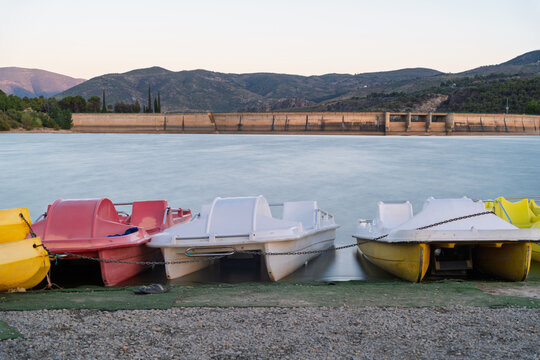 Pedal boats sit tethered on the shore of beznar reservoir, a dam created lake edged by mountains in granada, spain
