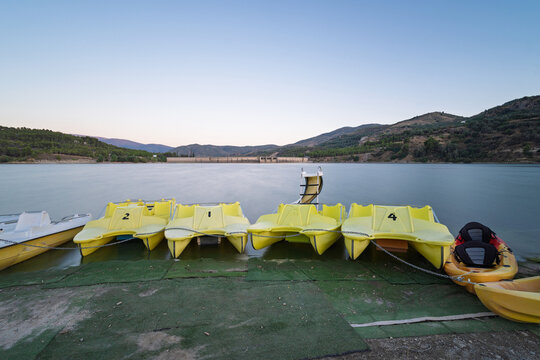 Yellow pedal boats and kayaks moored at beznar reservoir, granada, offering recreation activities on calm lake water with mountains