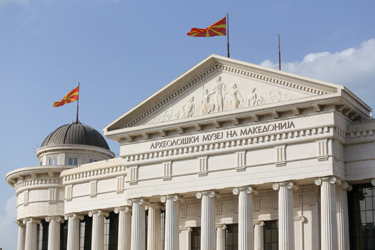 View of the Archaeological Museum of Macedonia with its neoclassical facade, columns, and flags against a clear blue sky in Skopje, Greater Skopje, North Macedonia.